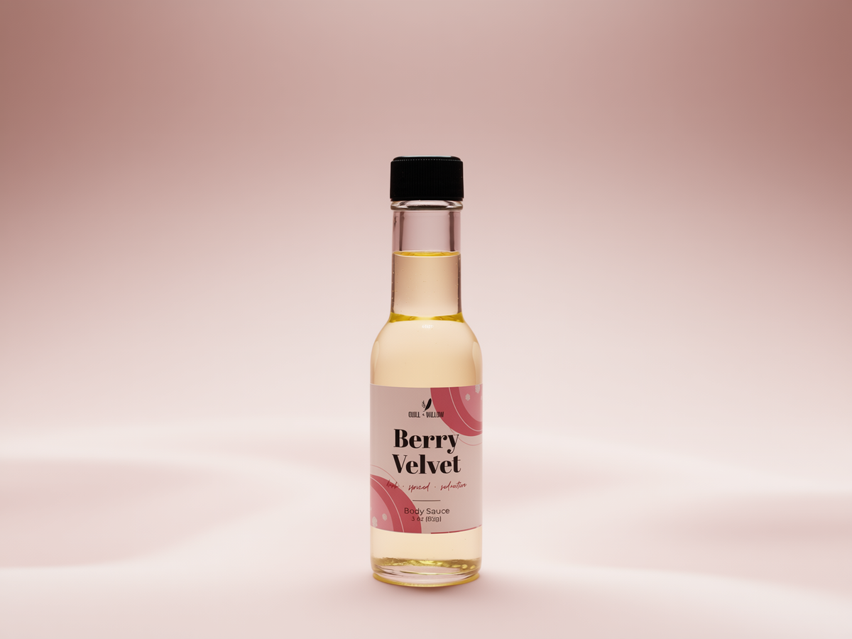 A small clear glass bottle of Berry Velvet body oil with a black cap and a pink and white label, centered on a soft pink gradient background.