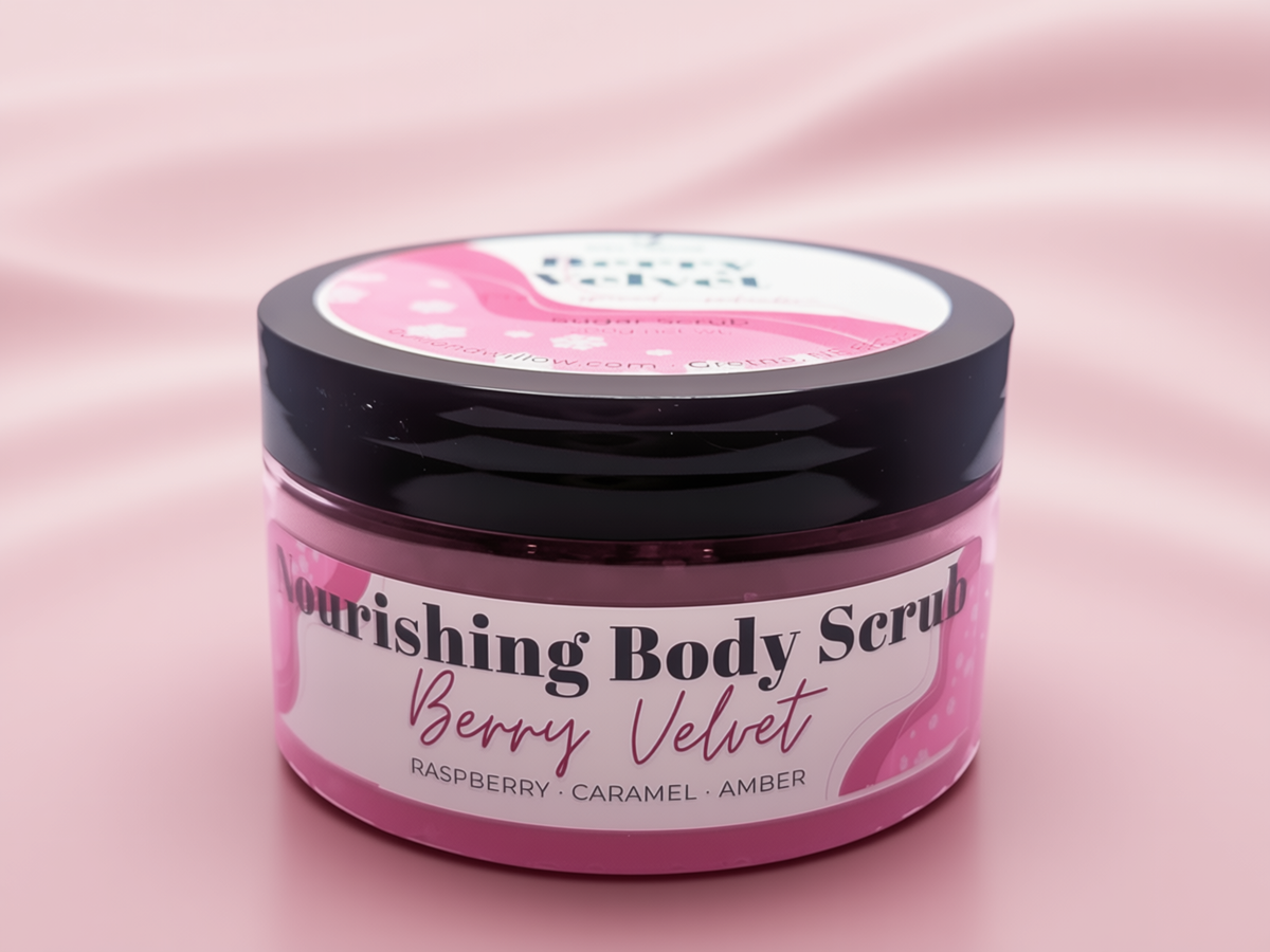 A jar of Nourishing Body Scrub in the Berry Velvet scent, featuring a pink label and black lid, set against a soft pink satin background.