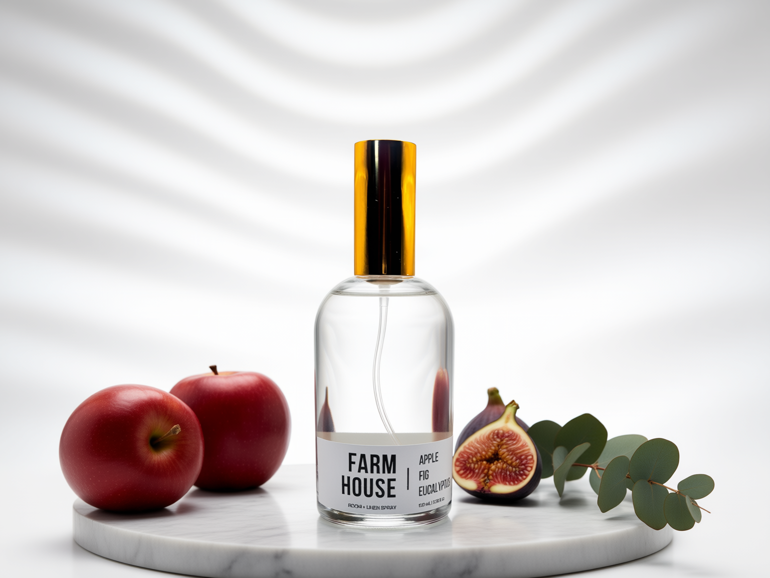A clear glass perfume bottle with a metallic gold cap and a white label reading 'FARMHOUSE APPLE, FIG Eucalyptus', styled on a round marble tray with red apples, a fig, and eucalyptus leaves against a white background with soft shadow patterns.