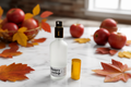 A frosted glass spray bottle labeled 'honey crisp' stands on a white marble surface, surrounded by red apples and autumn leaves in a softly lit indoor setting.