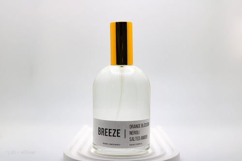 Clear bottle with gold lid labeled 'Breeze' room spray on a white background
