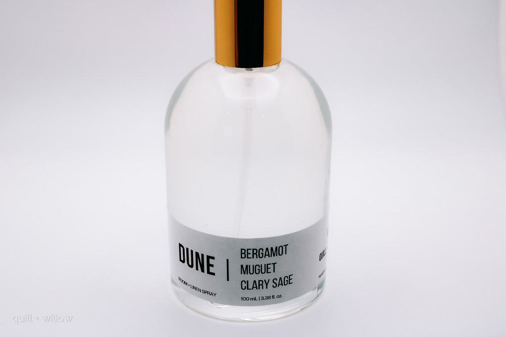 clear bottle with gold lid labeled Dune room spray scented with bergamot, muguet, and clary sage