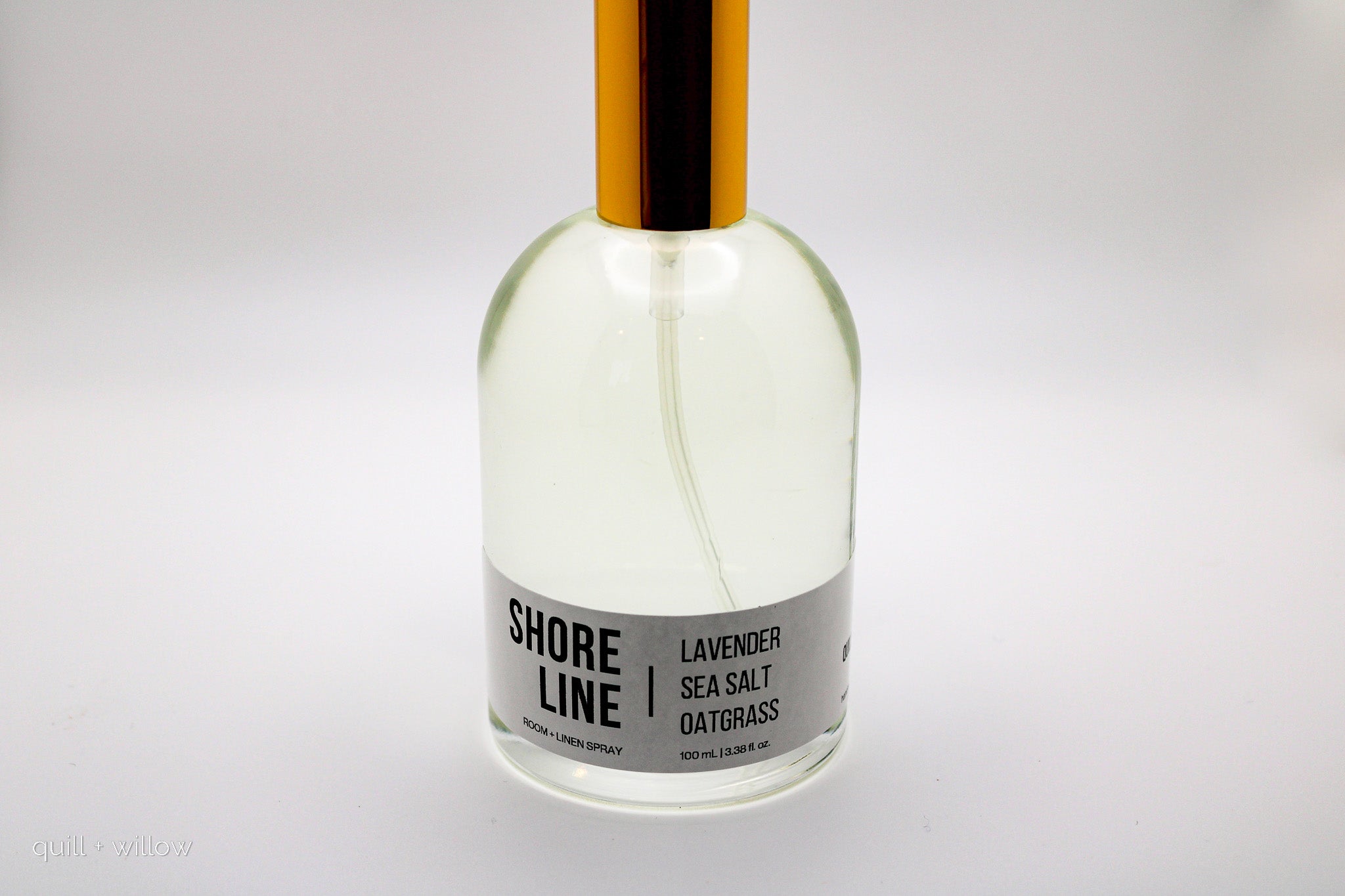 Clear bottle with a gold cap labeled 'Shore Line' room spray on a white background