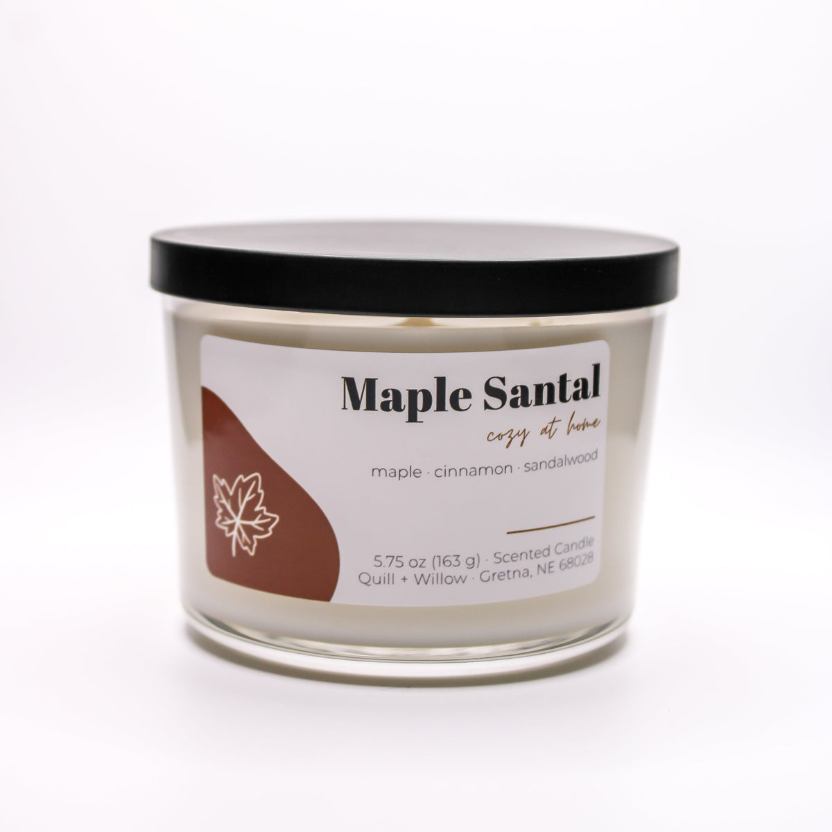 A single-wick scented candle in a clear glass jar labeled 'Maple Santal cozy home' on a plain white background