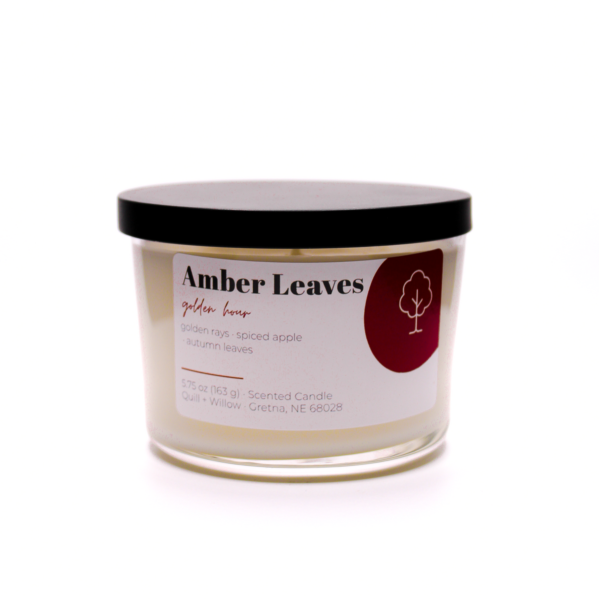 A scented candle in a clear glass jar with a black lid and a white label reading 'Amber Leaves' and 'Golden Hour', on a white background.
