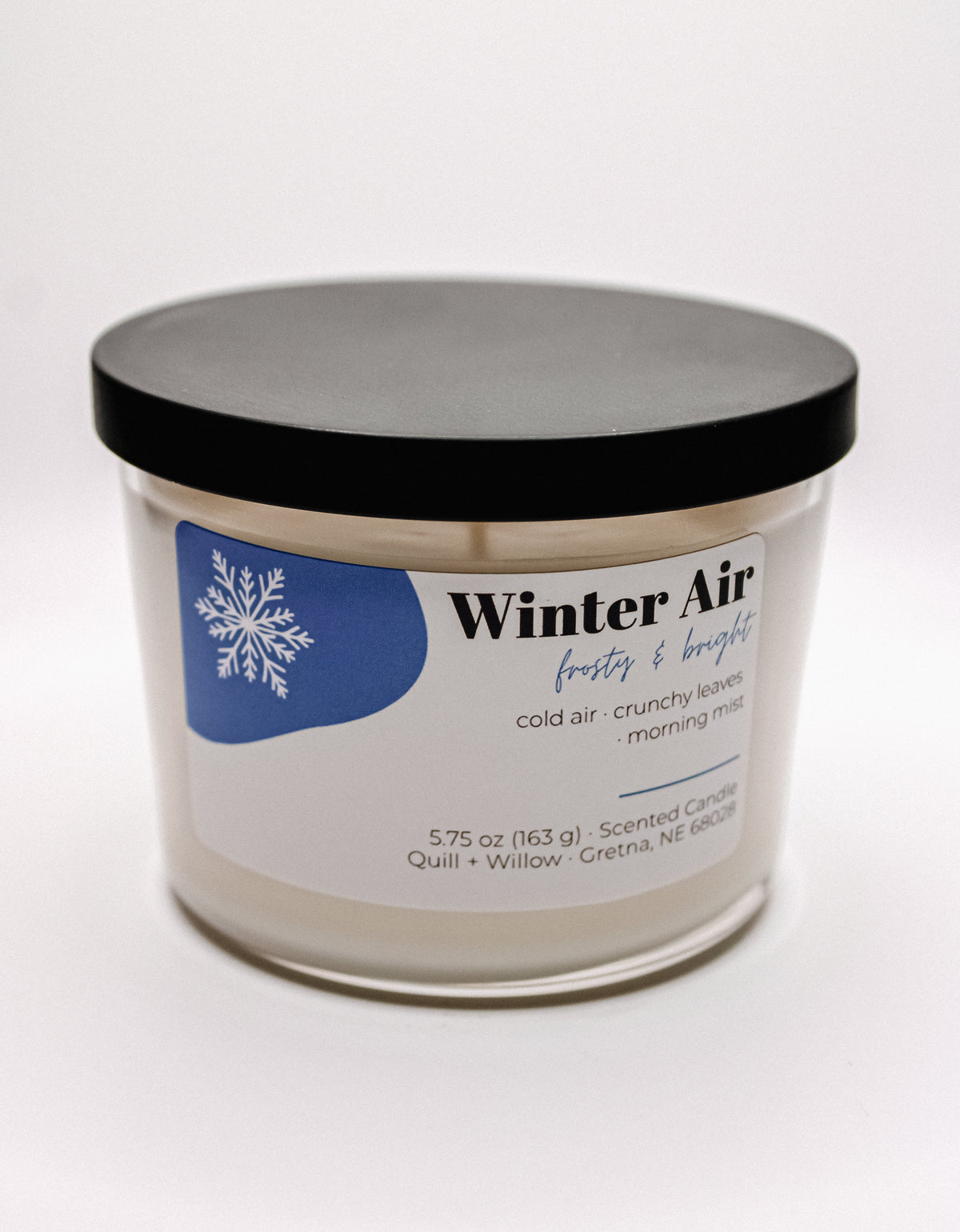 A clear glass jar candle labeled 'Winter Air' sits on a plain white background with a white and blue label.