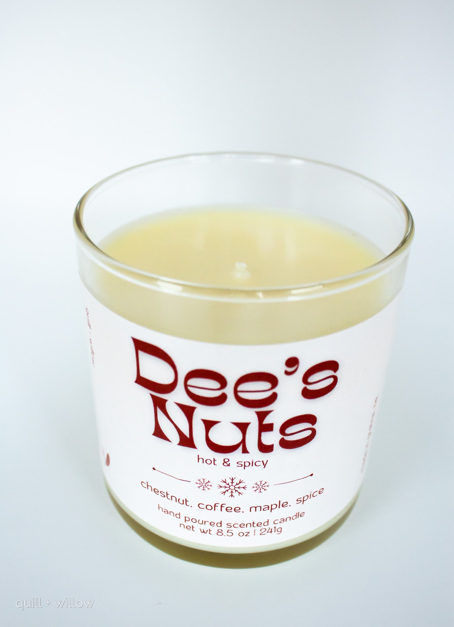 Candle in a glass jar labeled 'Dee's Nuts' on a white background