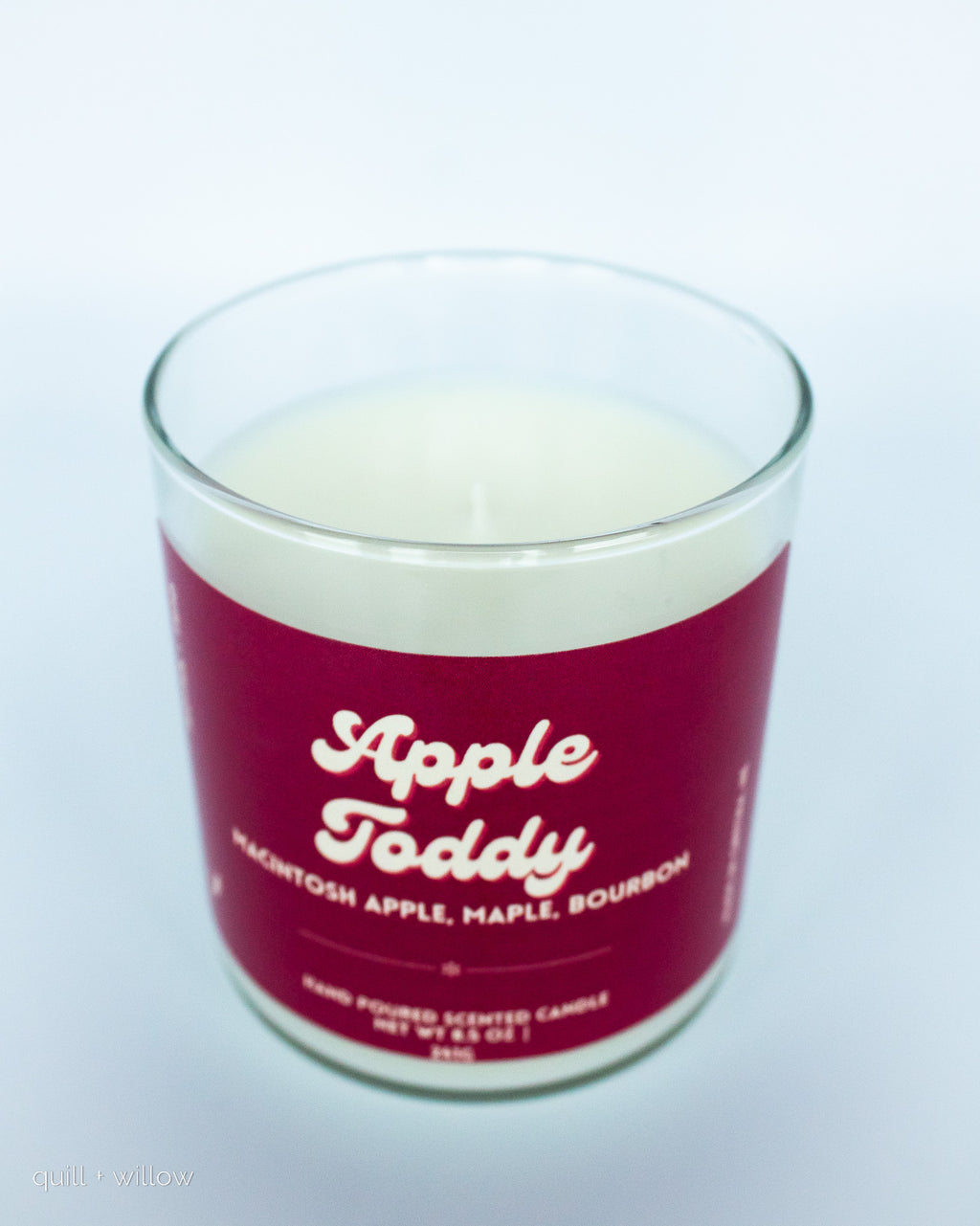 Candle in a glass jar with a red label reading 'Apple Toddy' on a white background