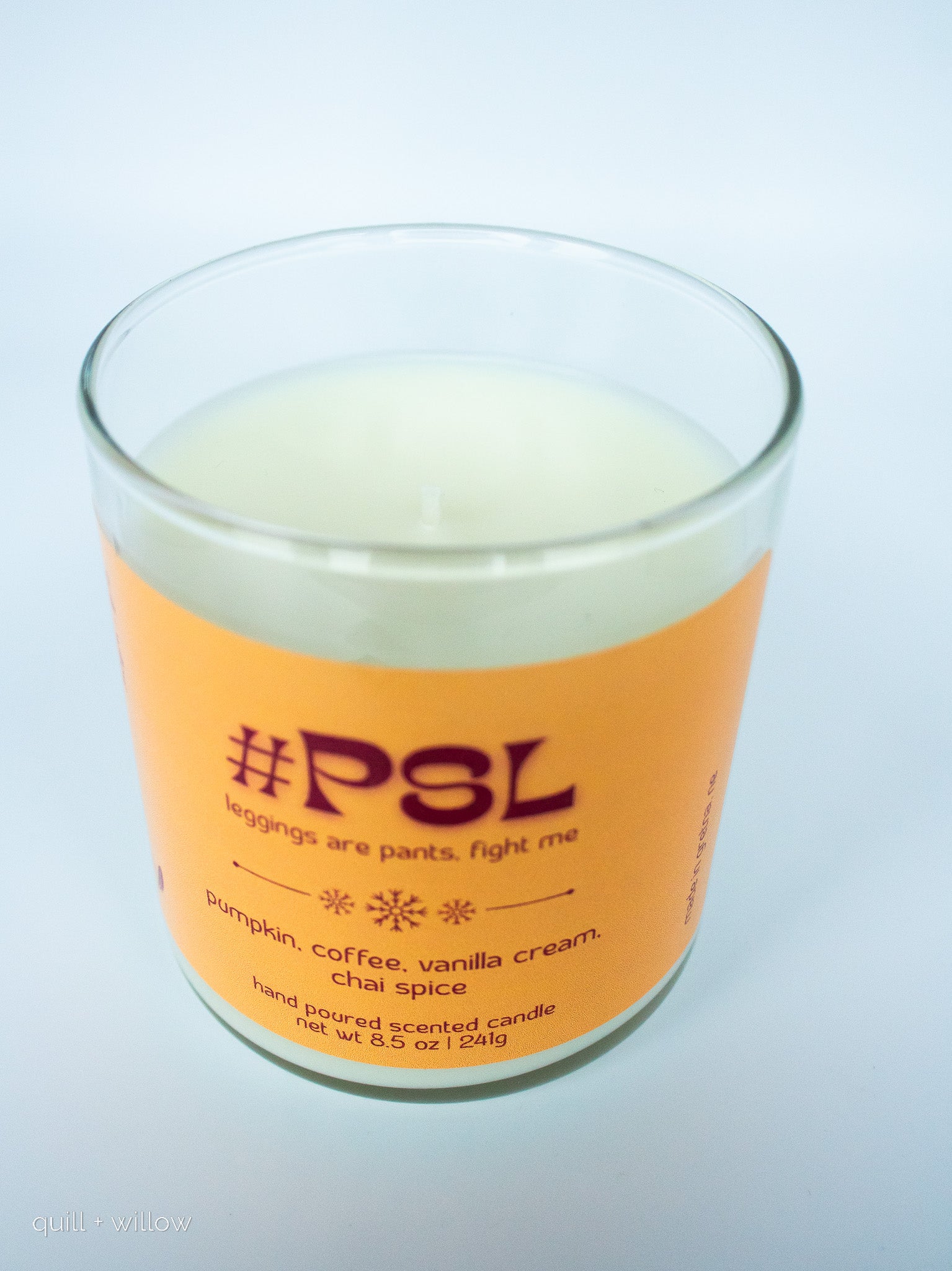 Candle with an orange label featuring the text 'PSL' on a light gray background