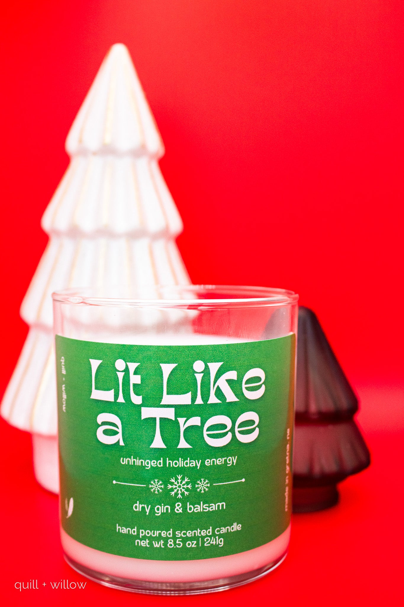 Candle labeled 'Lit Like a Tree' with Christmas tree decorations on a red background