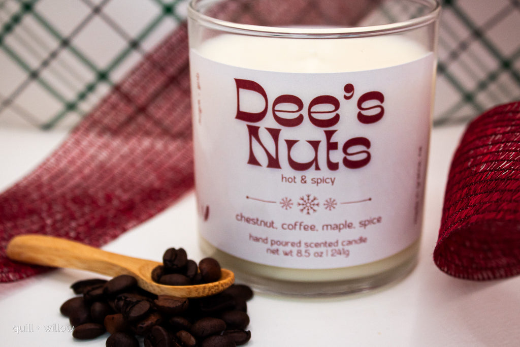 Candle labeled 'Dee's Nuts' with coffee beans and a wooden spoon on a white surface.
