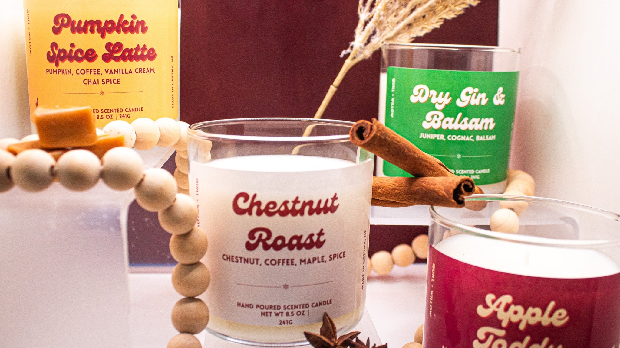 Candles with labels 'Pumpkin Spice Latte', 'Dry Gin & Balsam', and 'Apple Toddy' on a decorative surface.