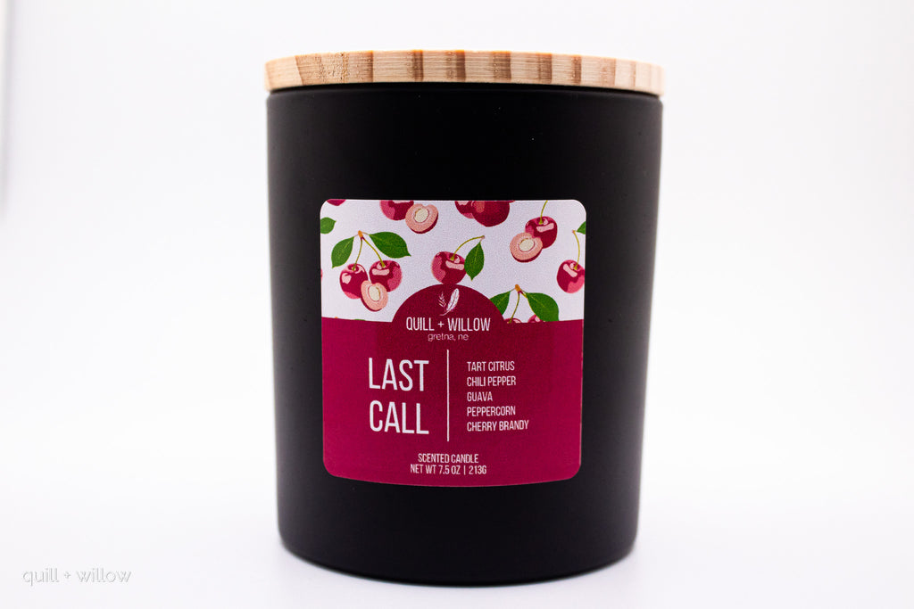 Black candle with a cherry-themed label on a white background