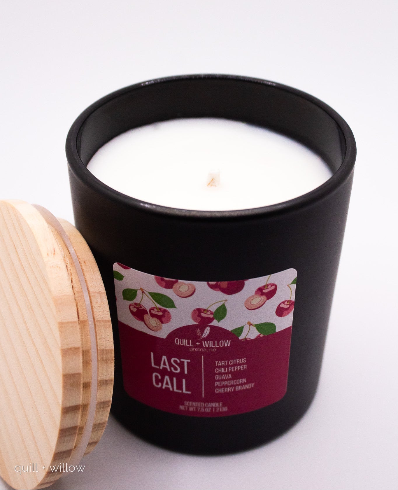 Candle in a black container with a decorative label on a white background