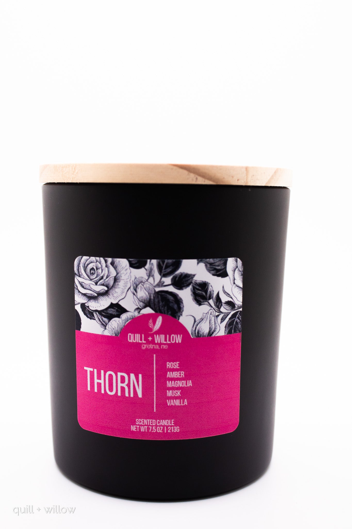 Black candle with a pink label featuring floral designs on a white background