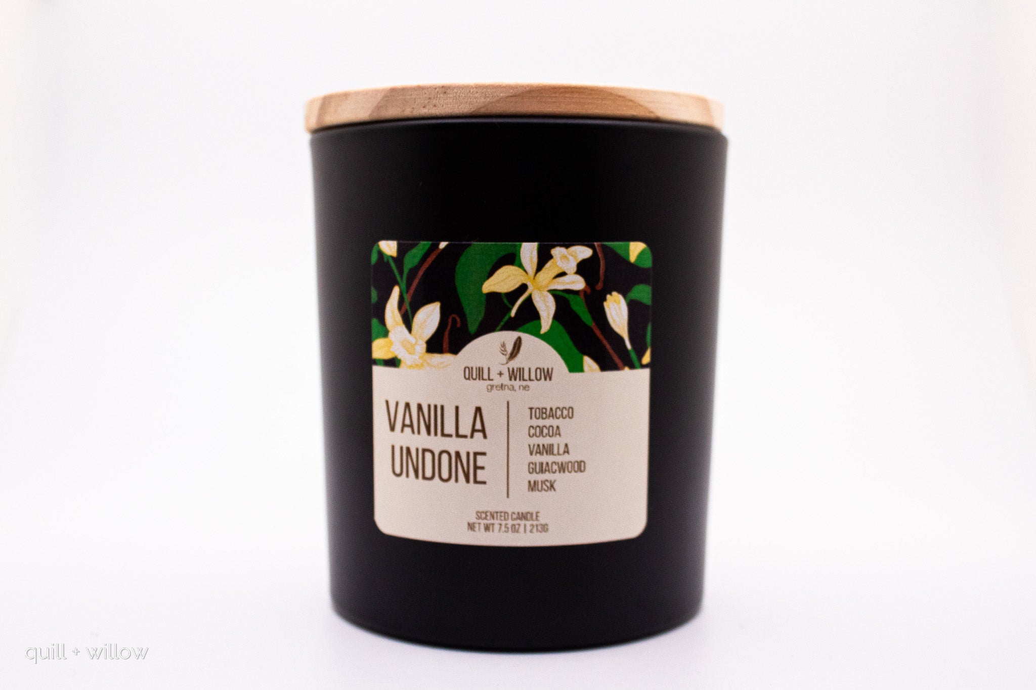 Black candle with a wooden lid and vanilla-scented label on a white background