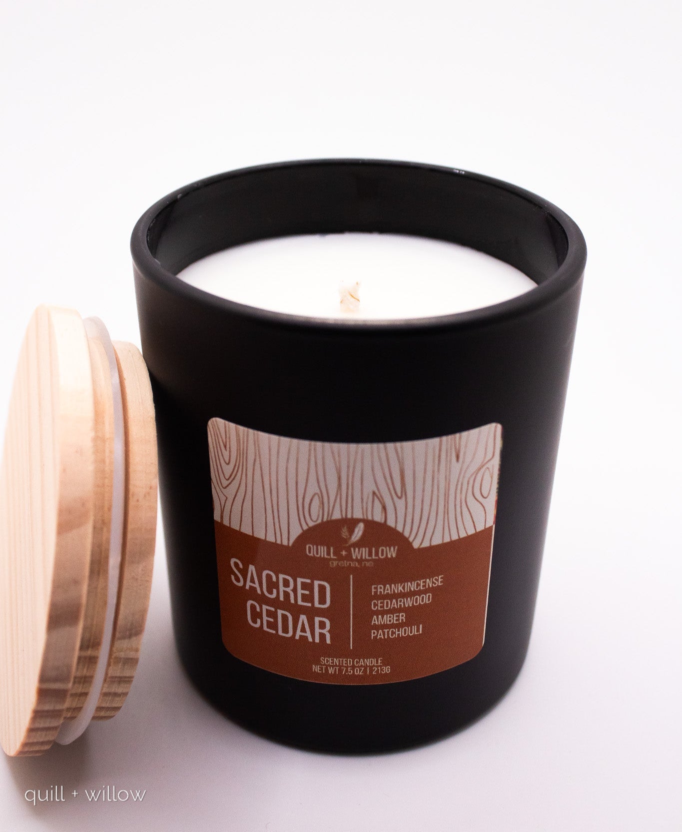 Black candle with a wooden lid and 'Sacred Cedar' label on a white background