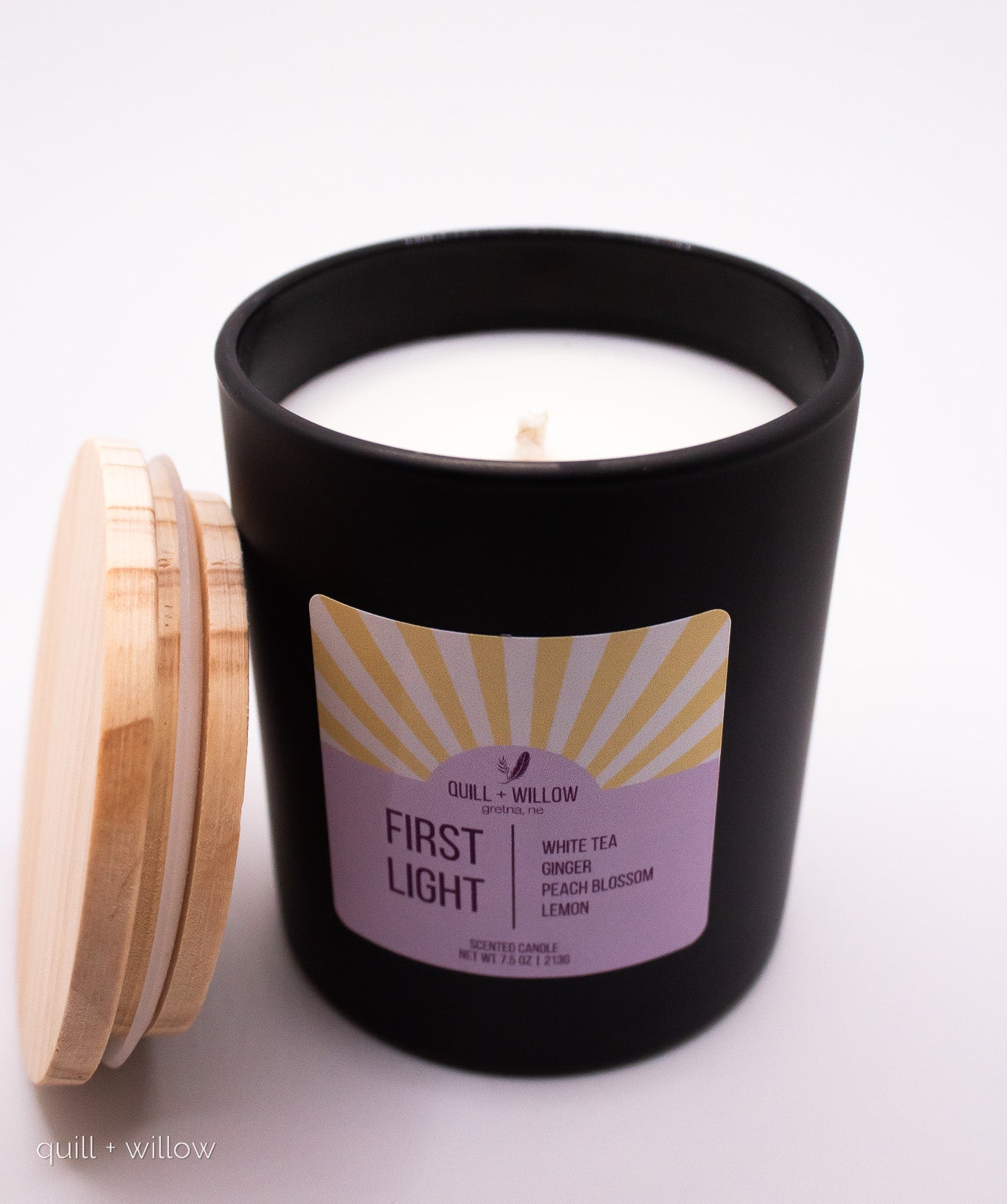Black candle jar with a wooden lid labeled 'First Light' on a white background