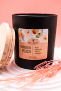 Black candle with a 'Forbidden Peach' label on a pink background