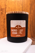 Candle labeled 'Sacred Cedar' with a wooden lid on a white surface against a wooden background.