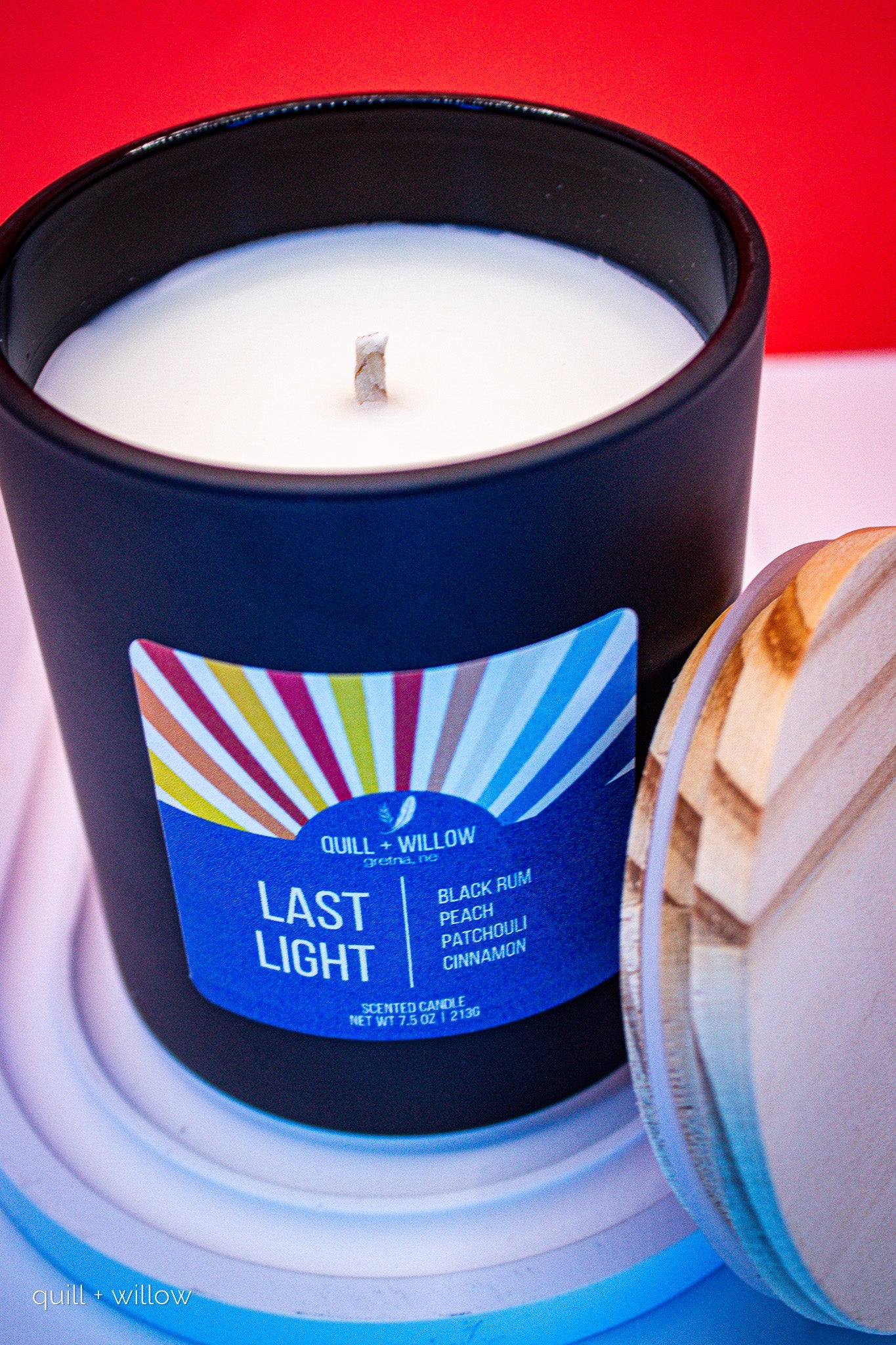Candle in a black container with a colorful label on a red and blue background