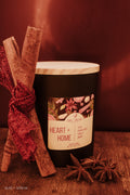 Candle labeled 'Heart + Home' with cinnamon stick and star anise on a wooden surface