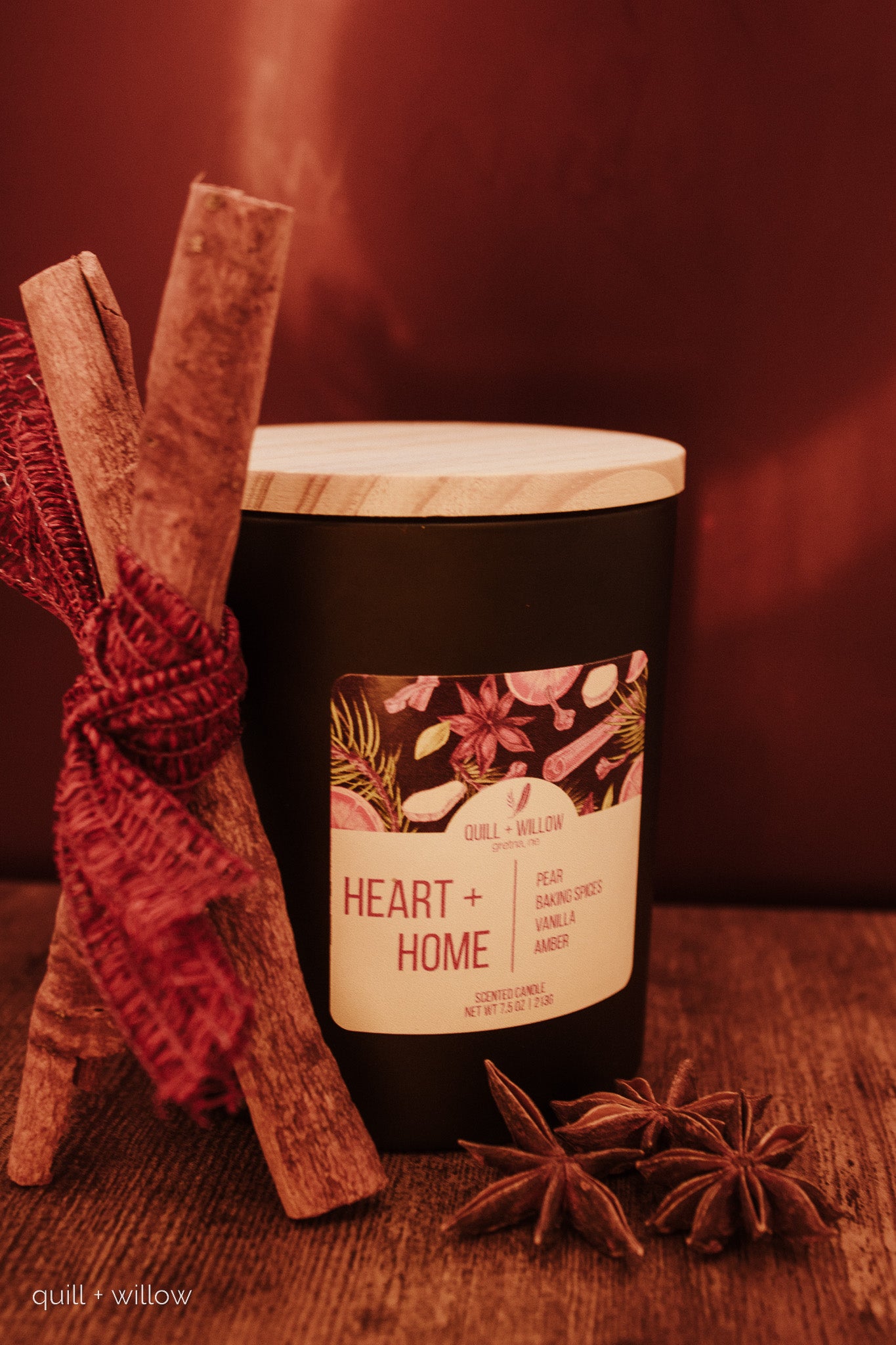 Candle labeled 'Heart + Home' with cinnamon stick and star anise on a wooden surface