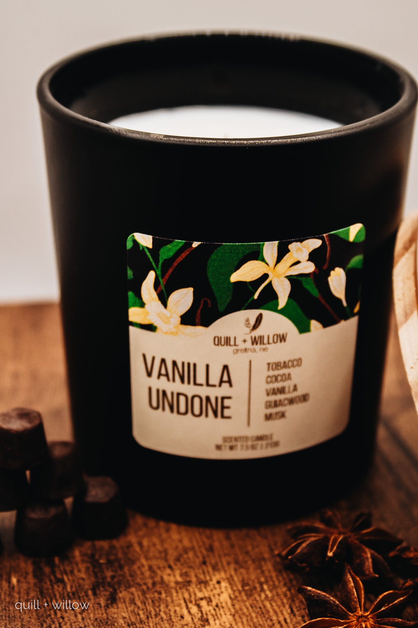 Black candle with a floral label on a wooden surface