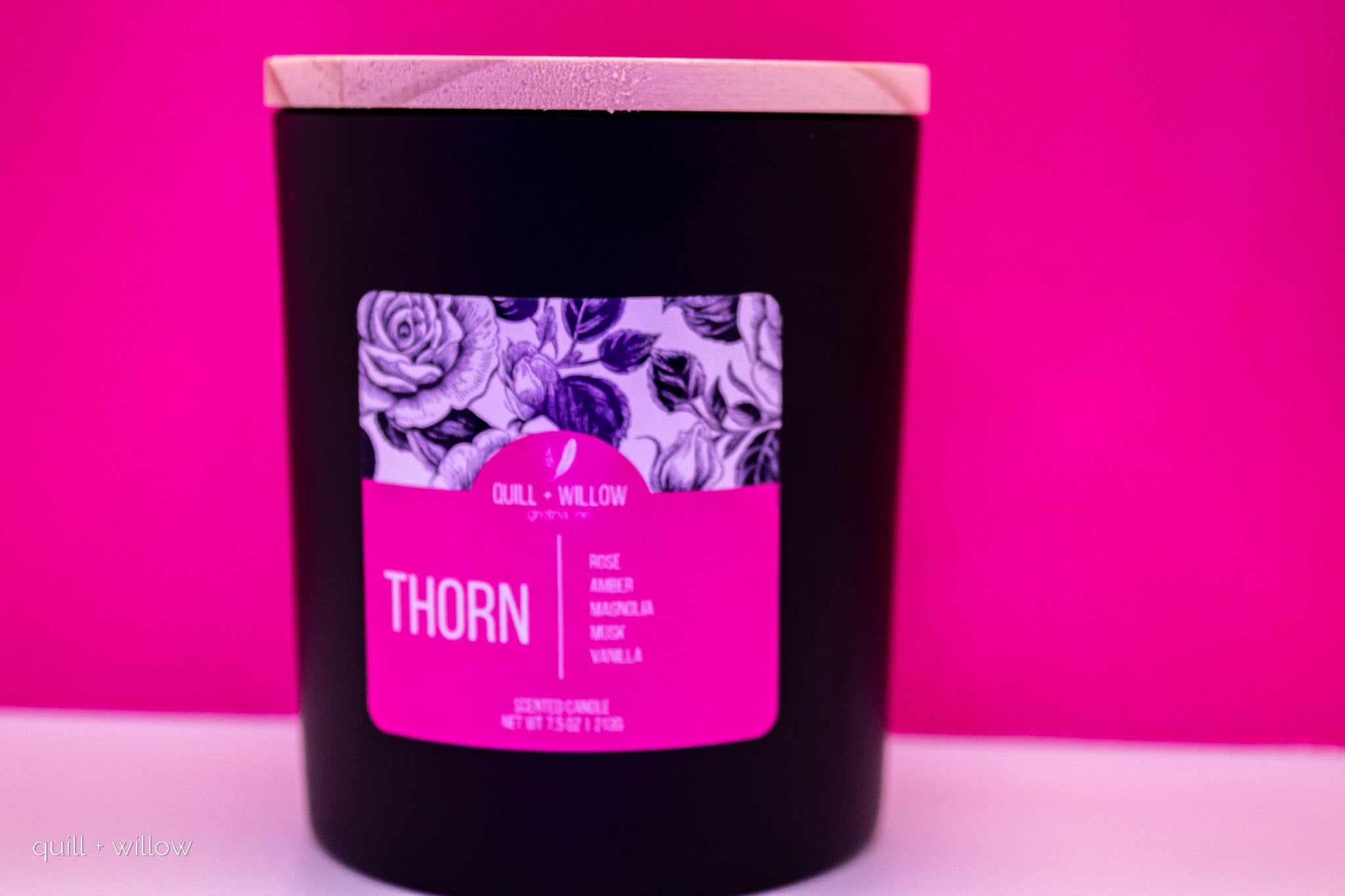 Black candle with a pink label featuring floral design on a pink background