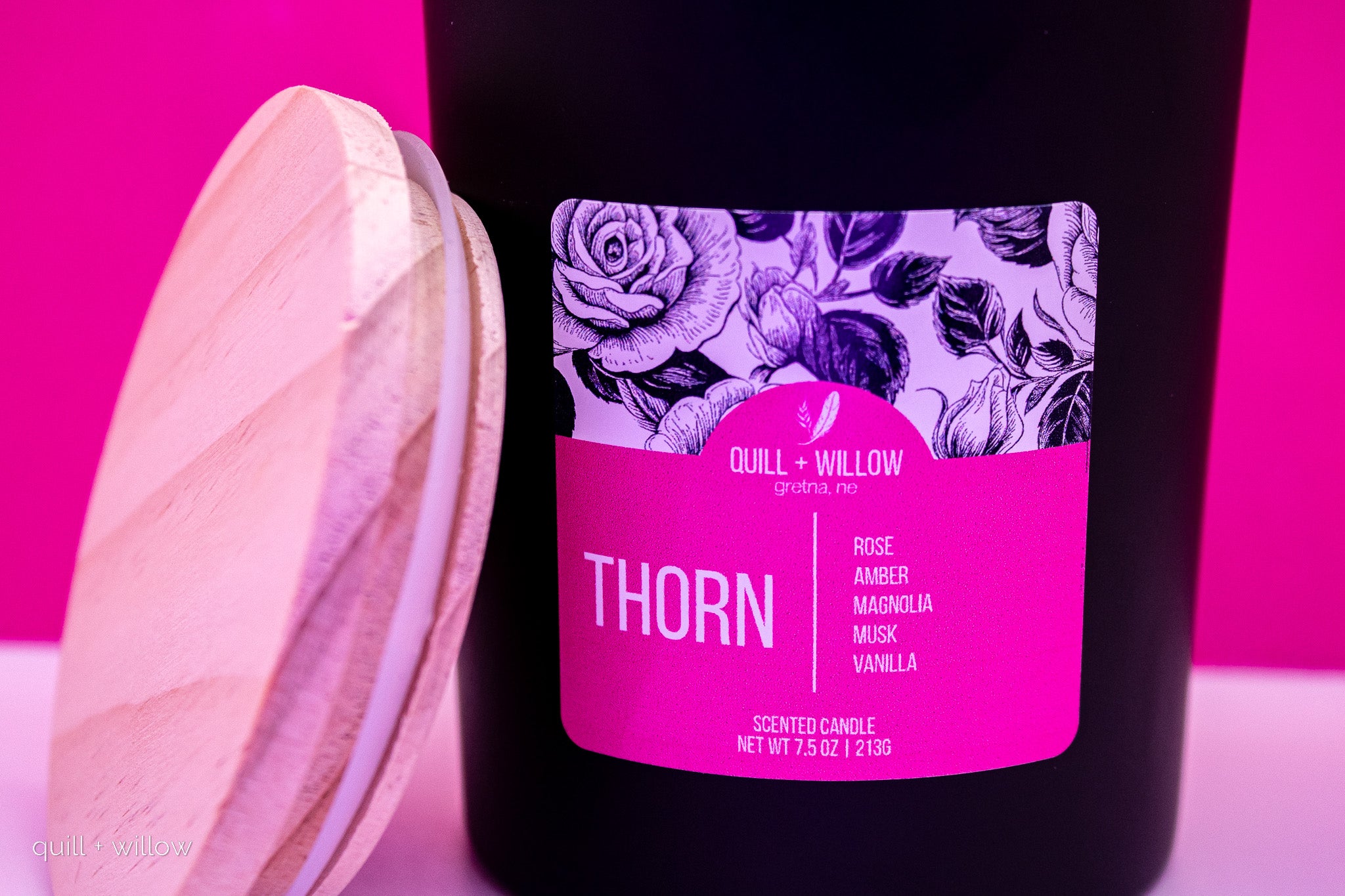 Black candle with a pink label featuring floral design and 'Quill + Willow' branding on a pink background.