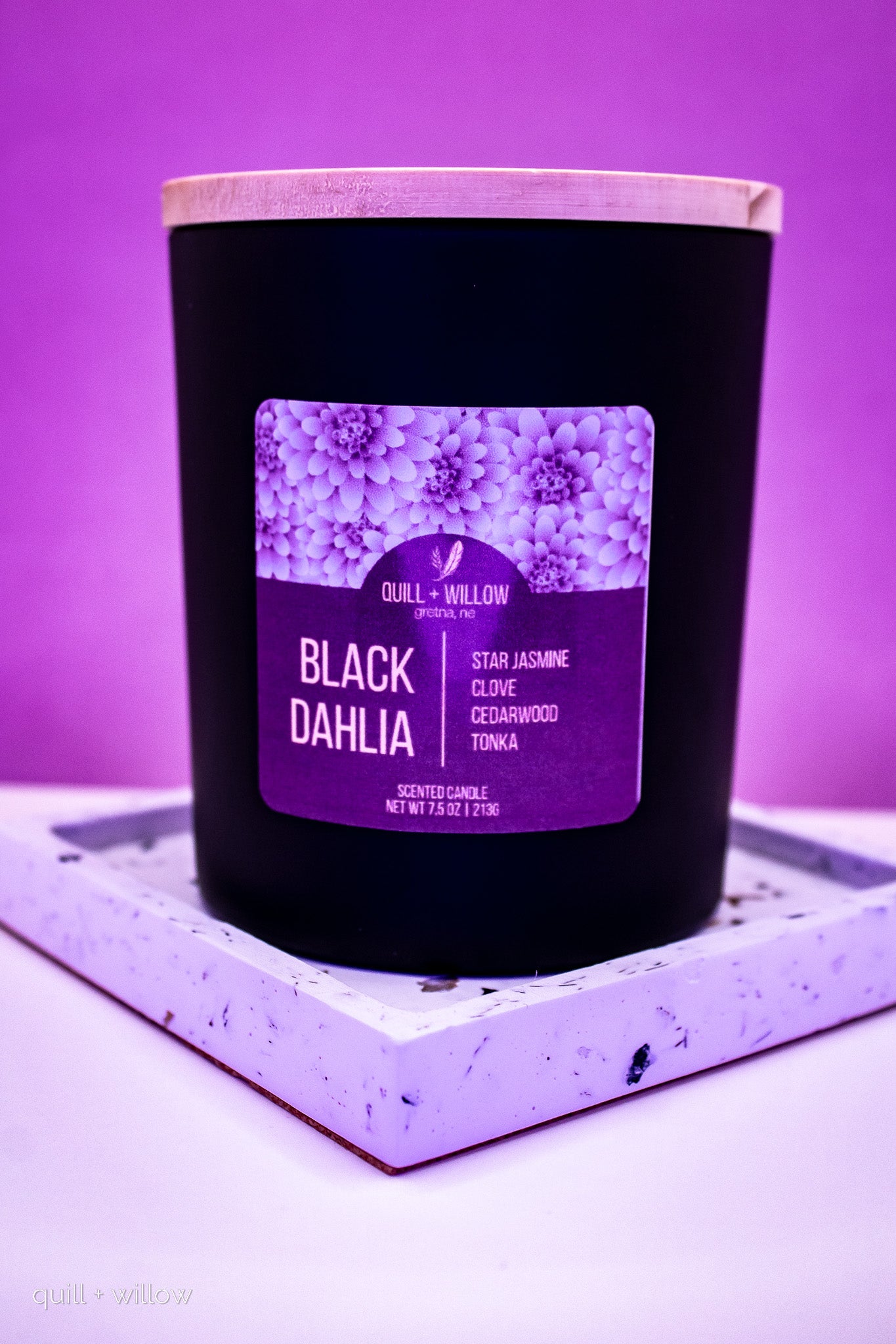 Black candle with a purple label on a white surface with a purple background